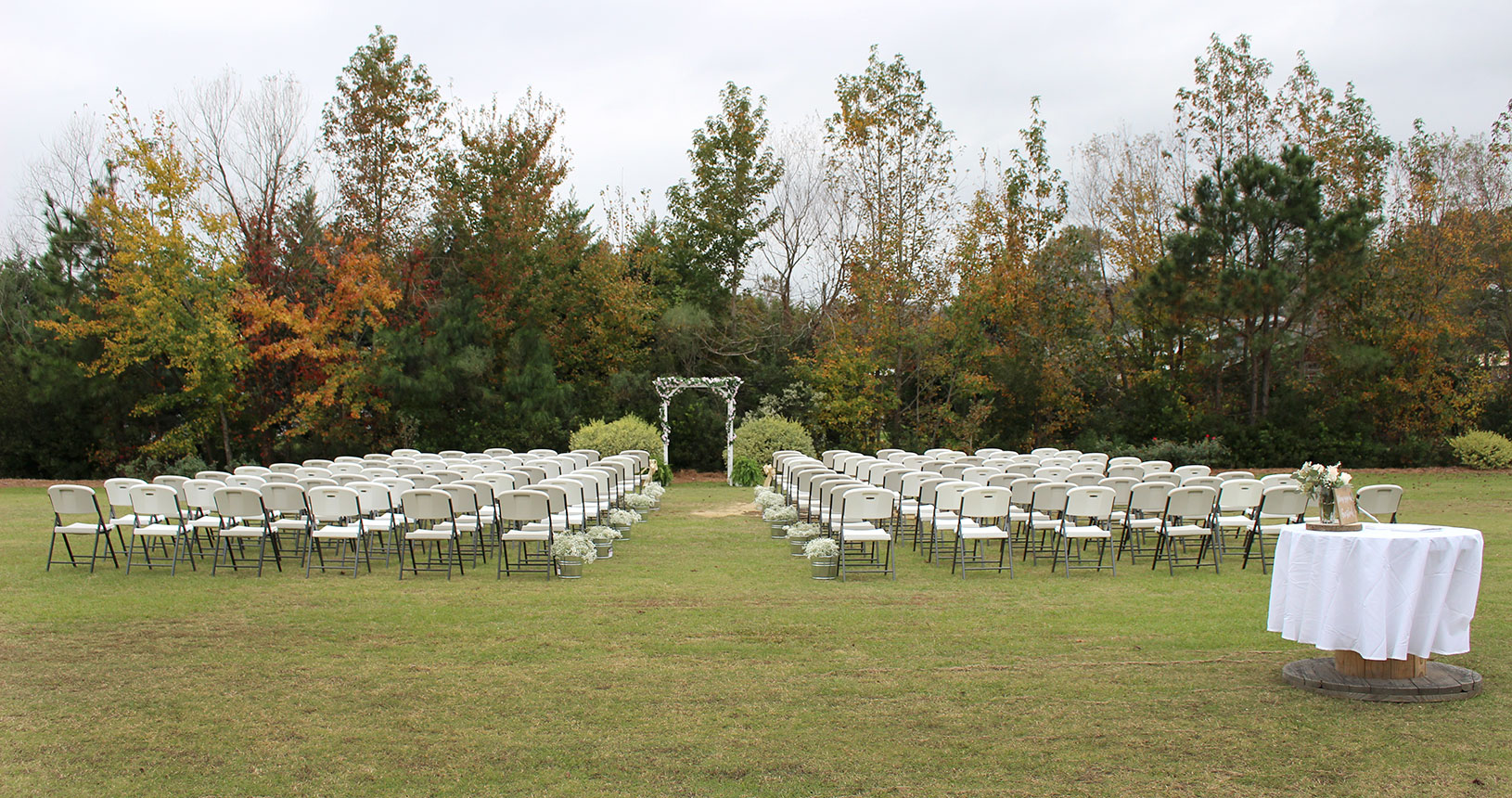 A wedding ceremony with white chairs and trees.